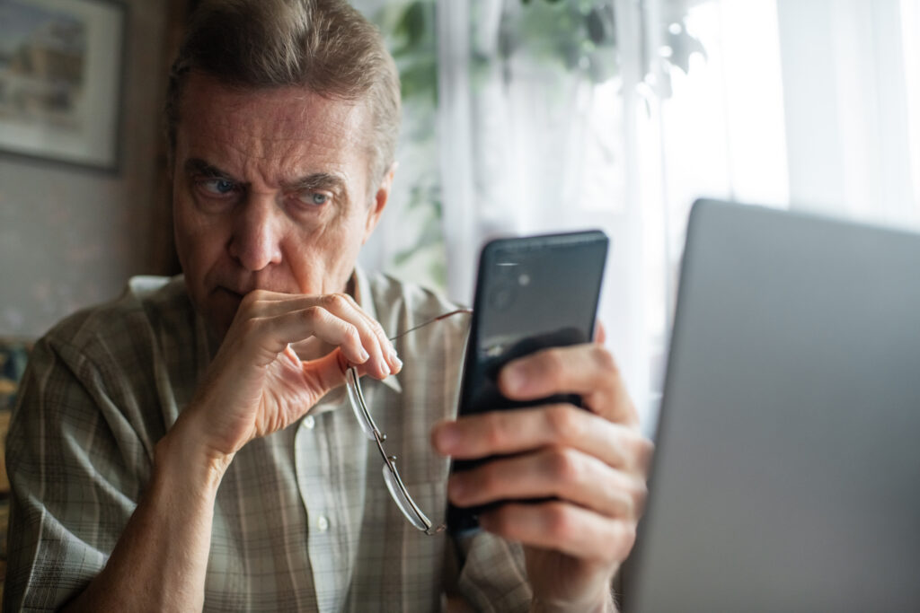 Senior man looking cautiously at smartphone
