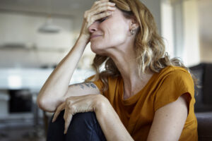 Sad woman with hands covering her face sitting on the floor at home
